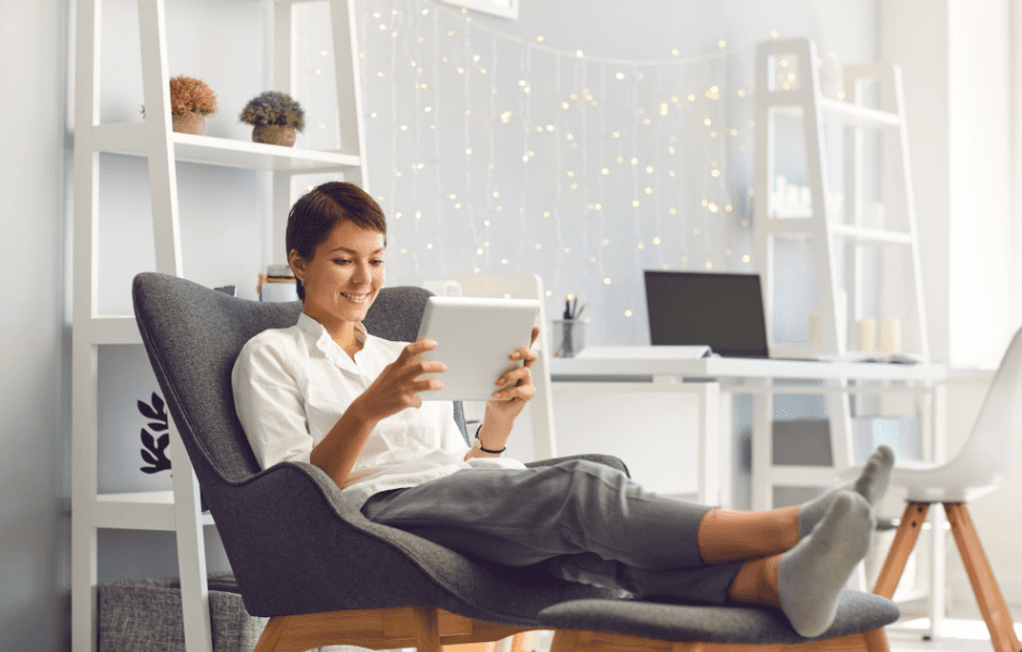 Happy and healthy young woman relaxing with feet up in chair on tablet